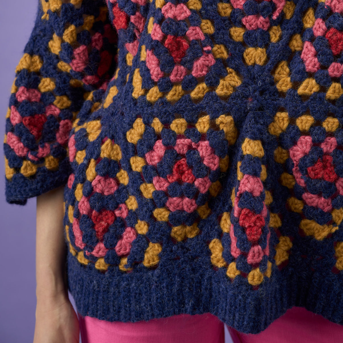 Close-up of a colorful crocheted garment with a geometric pattern on a purple background.