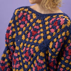 Colorful crocheted sweater with a geometric pattern against a purple background