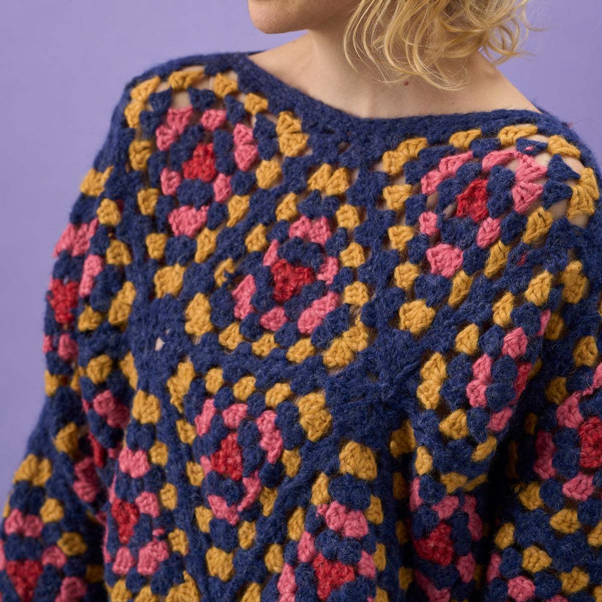 Colorful crocheted sweater with a geometric pattern against a purple background