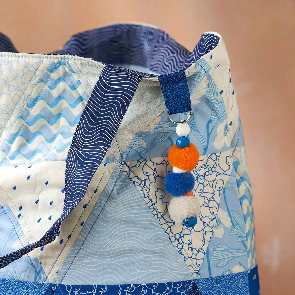 Close-up of a baby carrier with blue and white patterns and colorful pom-pom decorations.