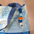 Close-up of a baby carrier with blue and white patterns and colorful pom-pom decorations.