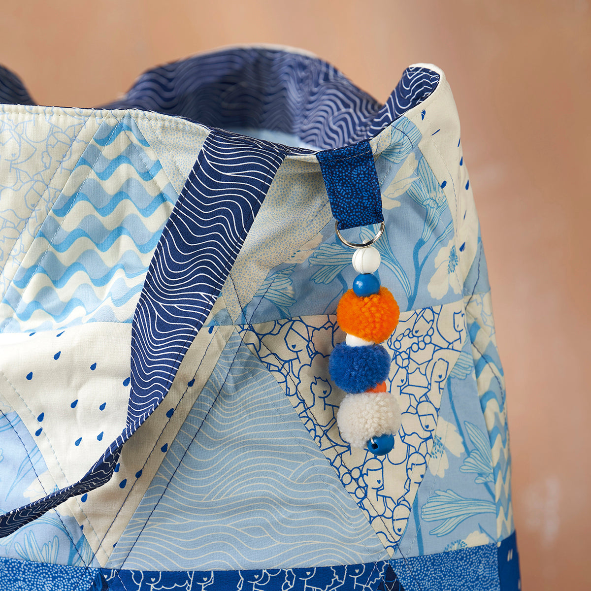 Close-up of a baby carrier with blue and white patterns and colorful pom-pom decorations.