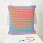 Colorful striped pillow on a white surface with coloured pens next to it.