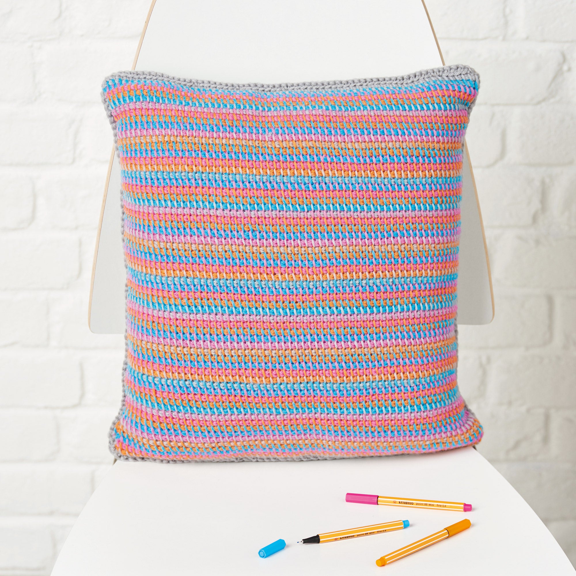 Colorful striped pillow on a white surface with coloured pens next to it.