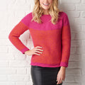 A smiling person wearing a vibrant pink and orange textured sweater and black leather skirt stands against a white brick wall, conveying a cheerful and stylish tone.