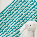 Teal and white chevron patterned blanket with a plush bunny toy on a light background