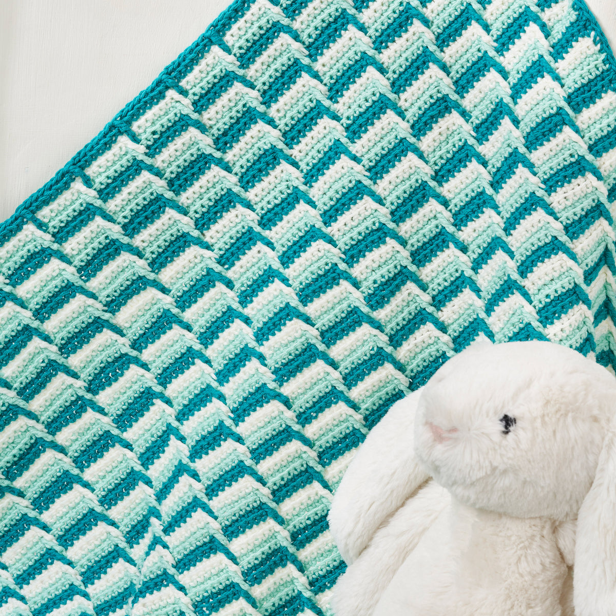 Teal and white chevron patterned blanket with a plush bunny toy on a light background