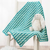 Teal and white patterned blanket draped over a chair with a plush toy on top.