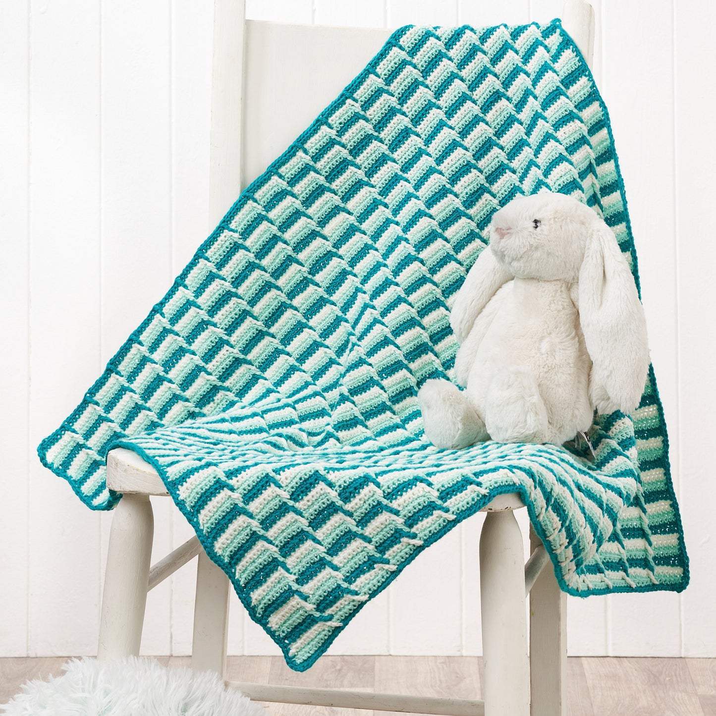 Teal and white patterned blanket draped over a chair with a plush toy on top.