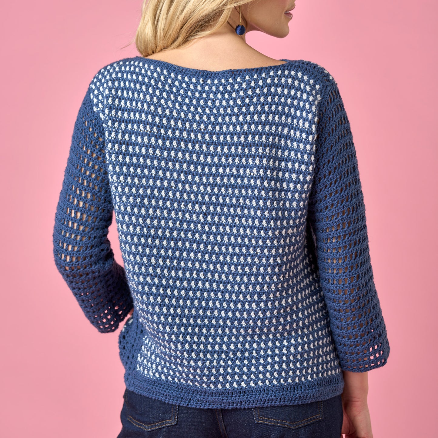 Blue crochet sweater worn by a person on a pink background