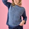Woman wearing a blue crochet sweater against a pink background