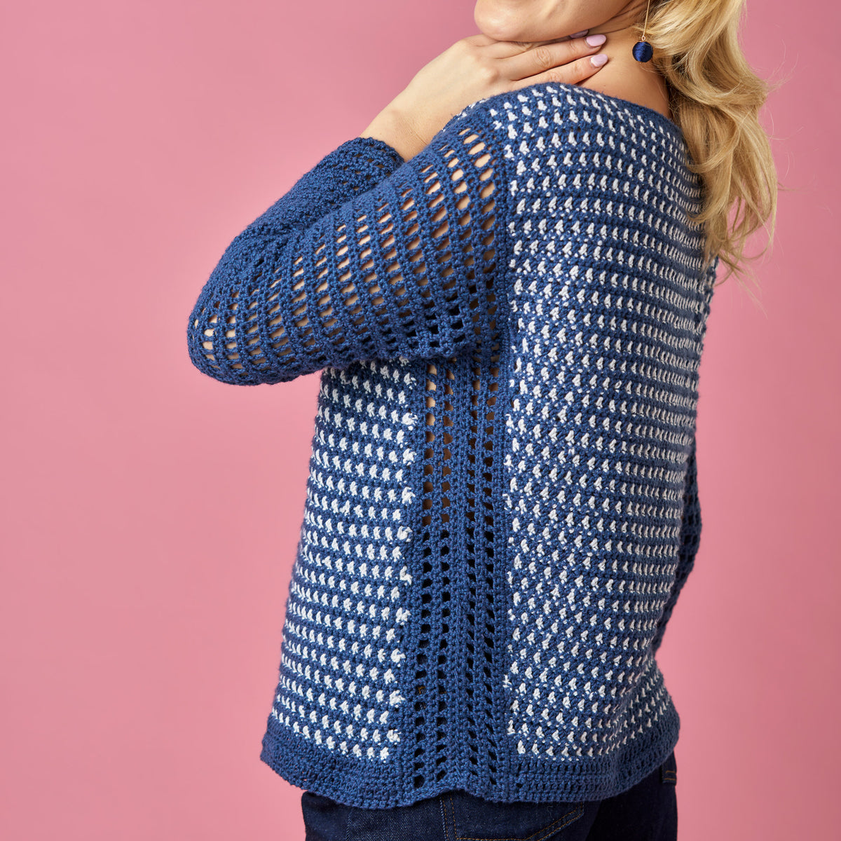 Blue crochet cardigan worn by a person on a pink background