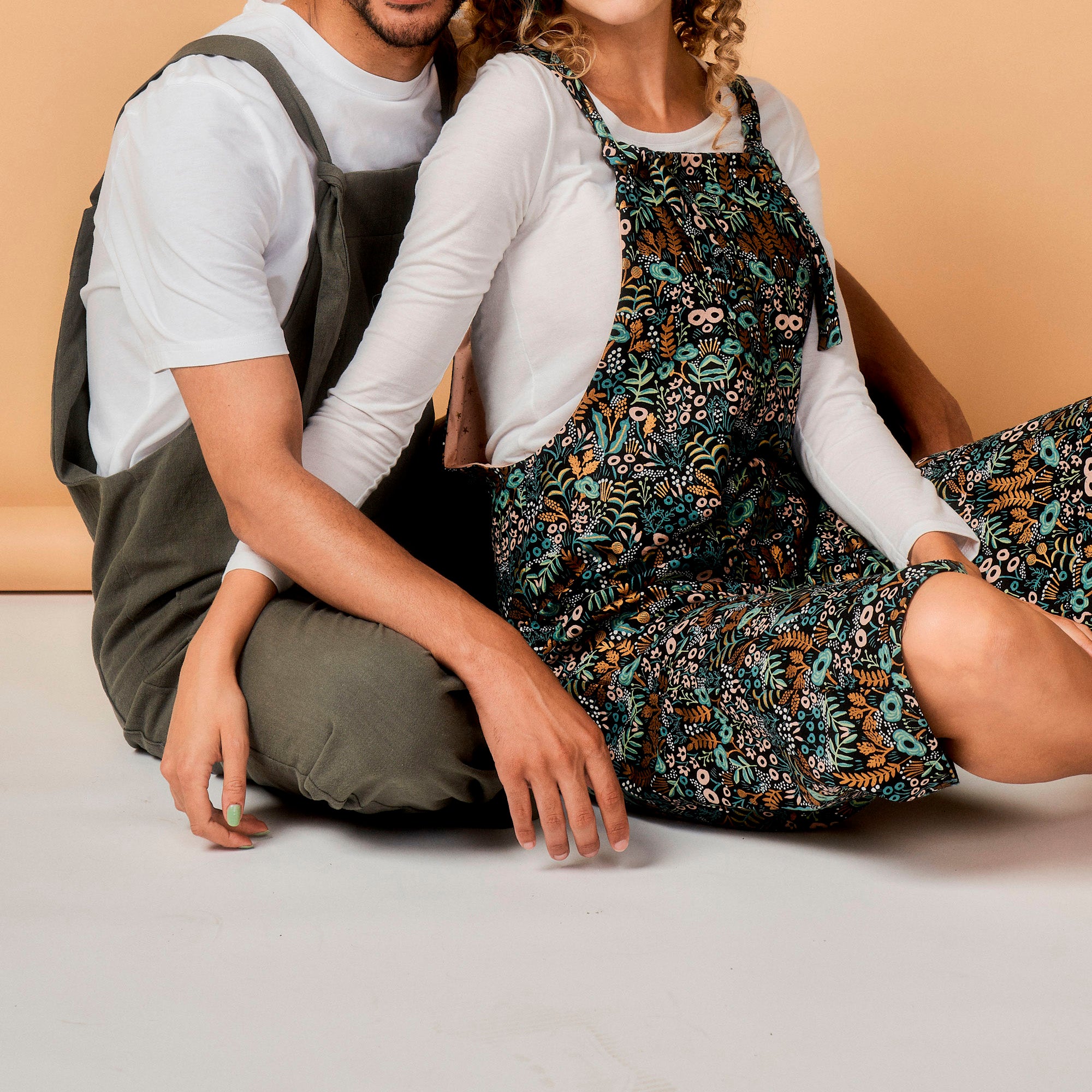 Two people wearing floral aprons sitting on a light-colored floor.