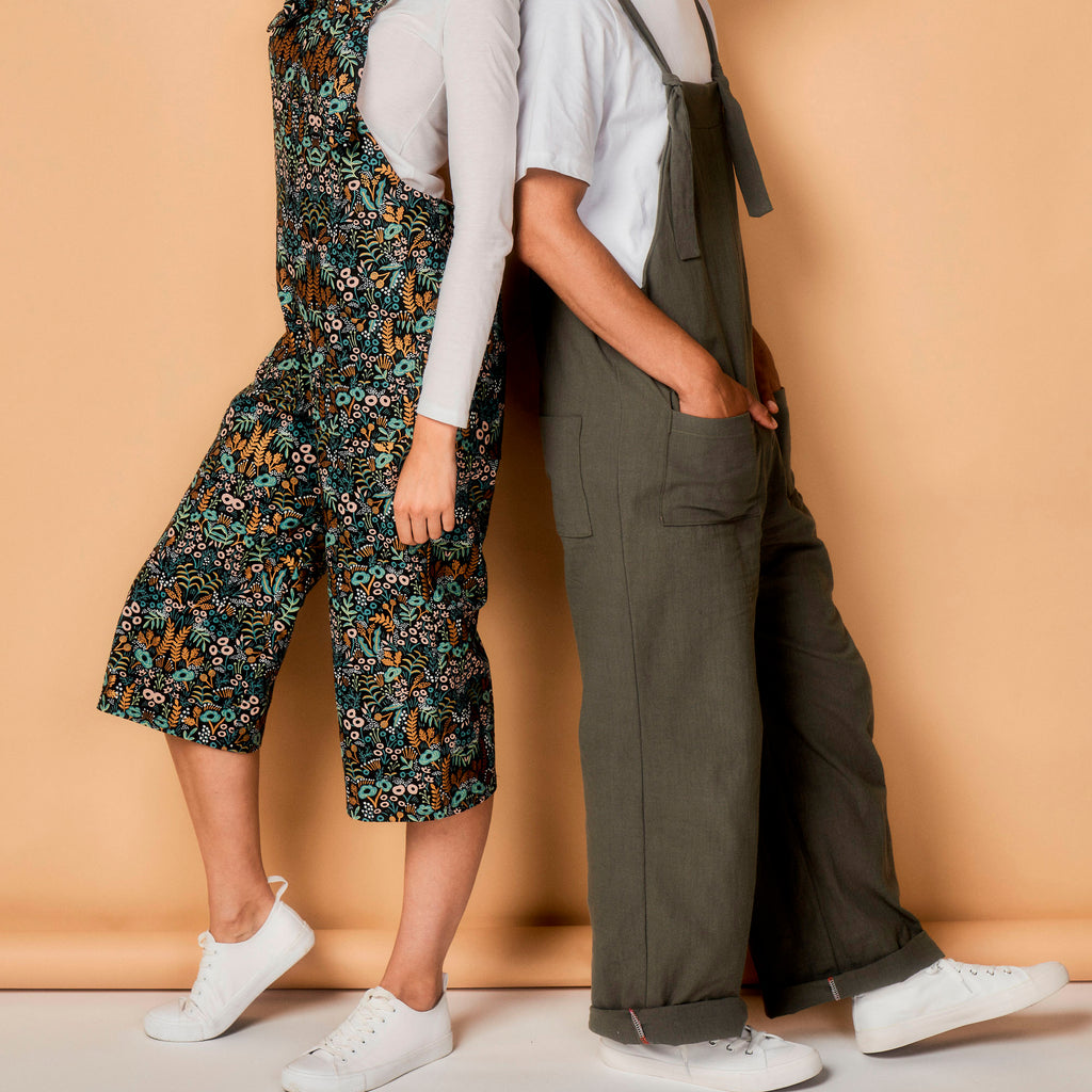 Two people wearing overalls against a beige background