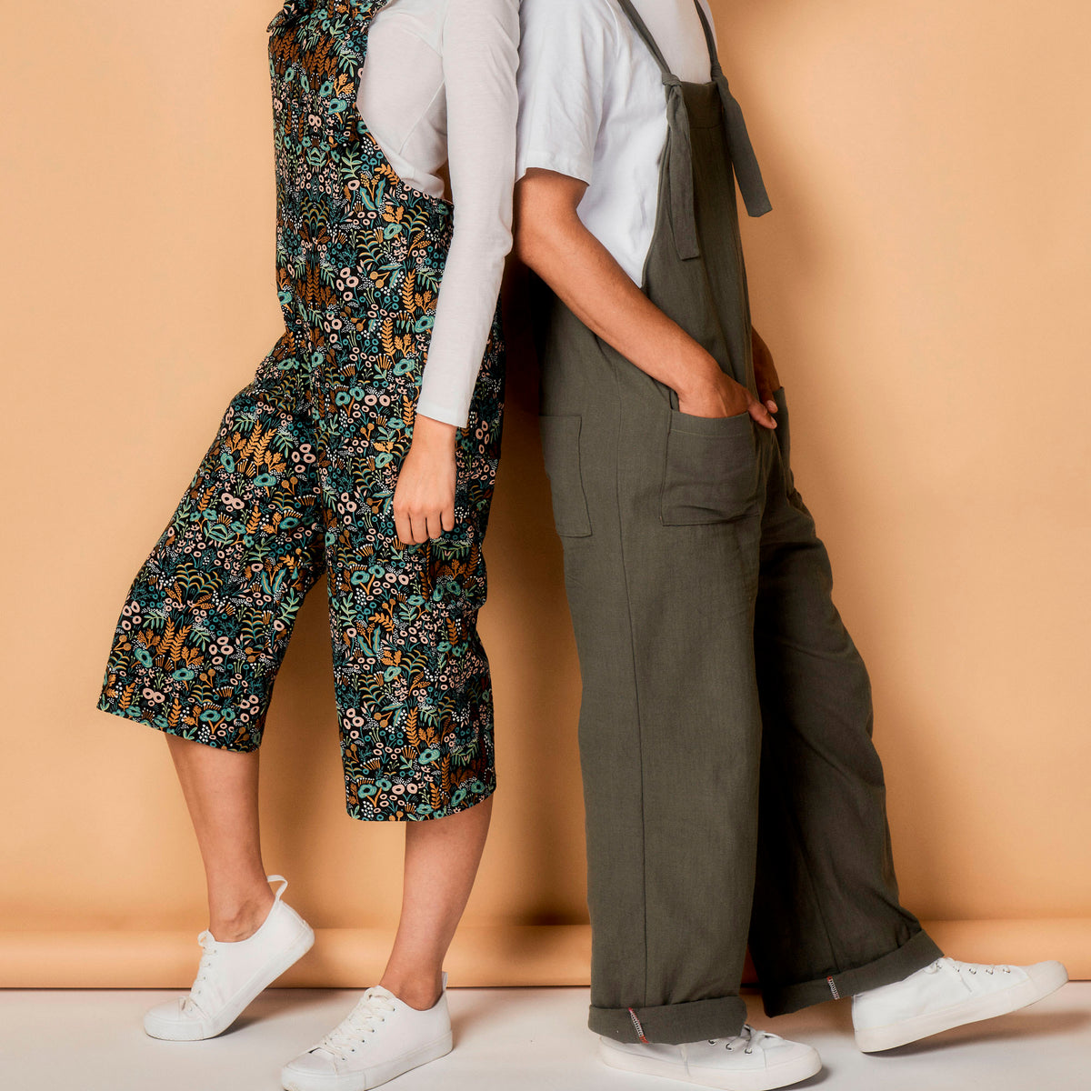 Two people wearing overalls against a beige background
