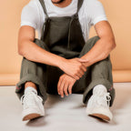 Person wearing green overalls and white sneakers sitting on a beige surface.