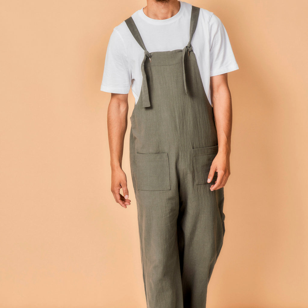 Person wearing green overalls and a white t-shirt on a beige background