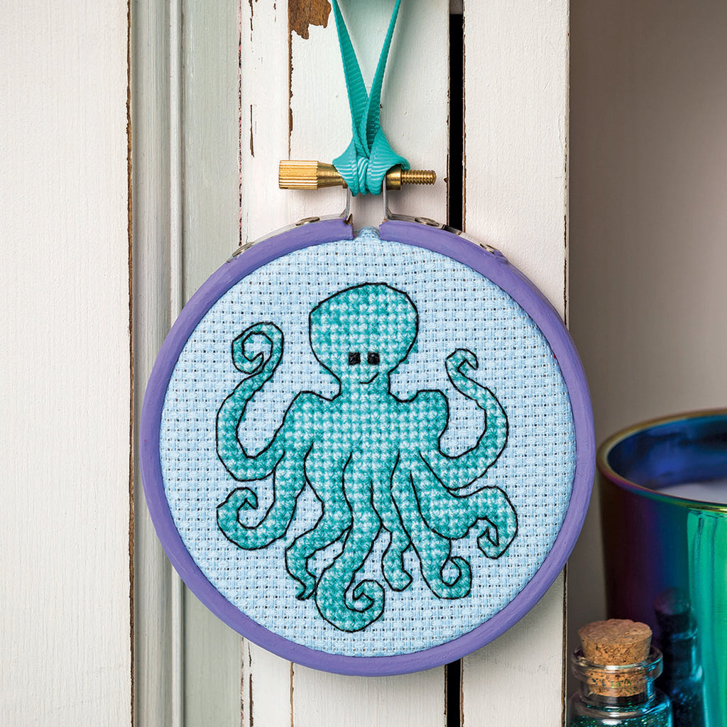 Embroidery hoop with a blue octopus design on a light blue background, hanging against a white wall.