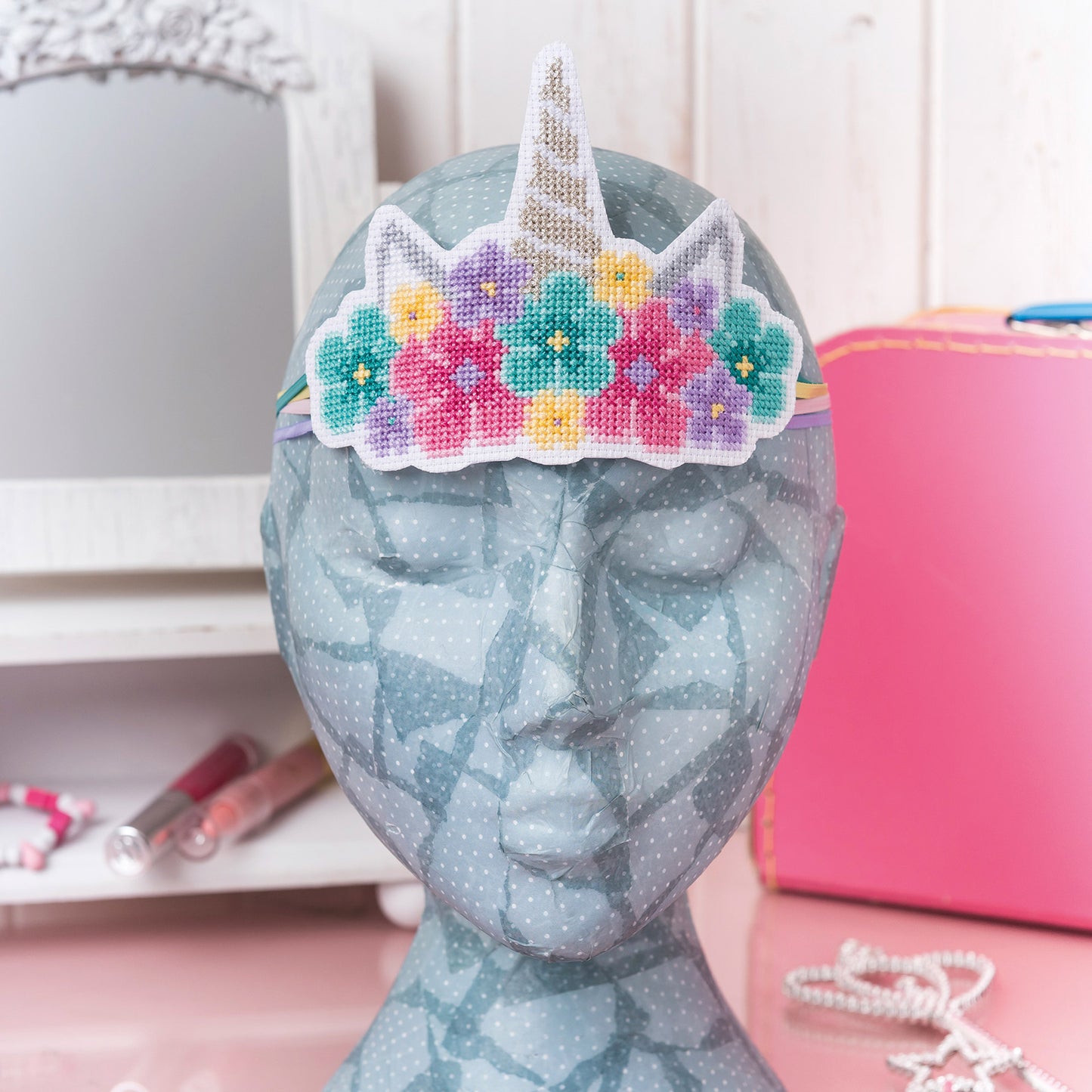 Decorative head with a floral unicorn horn headband on a pink surface.