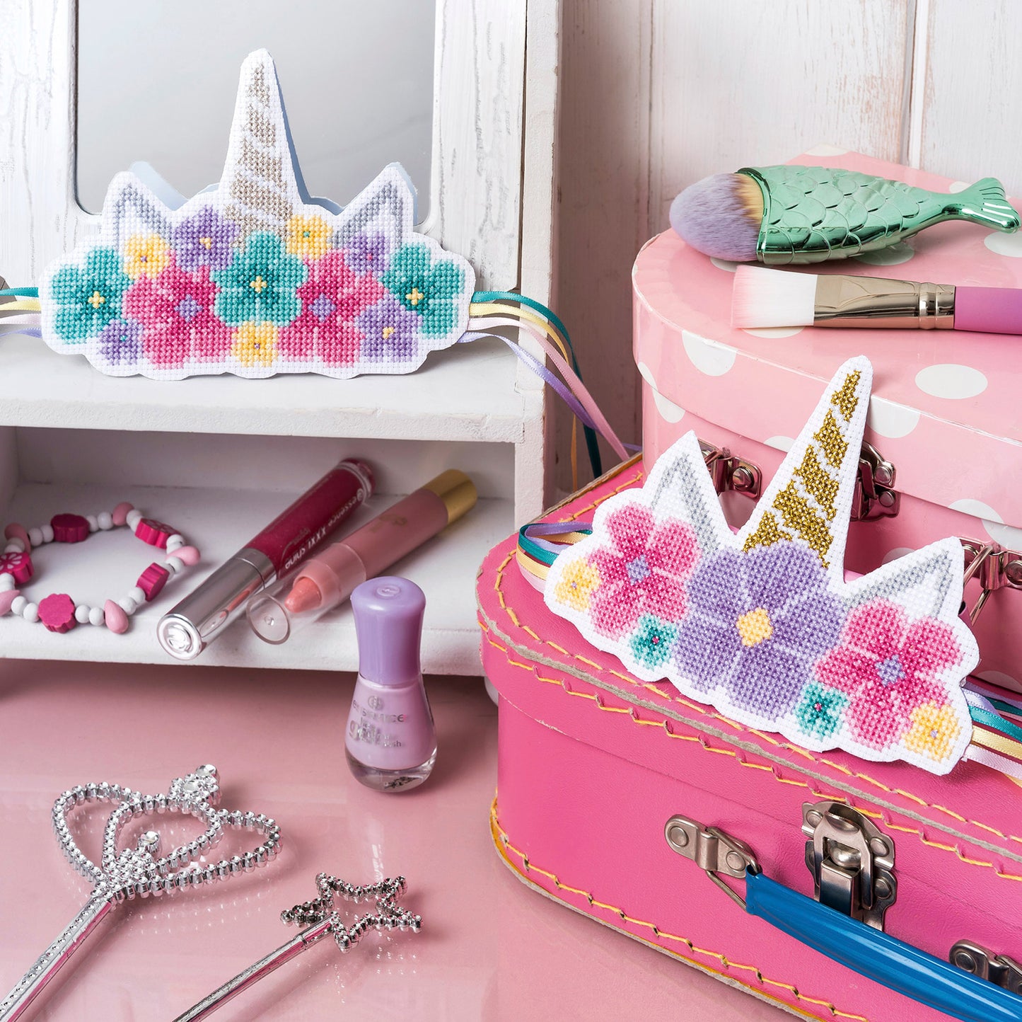 Decorative unicorn headbands with floral patterns on a pink suitcase with makeup items.
