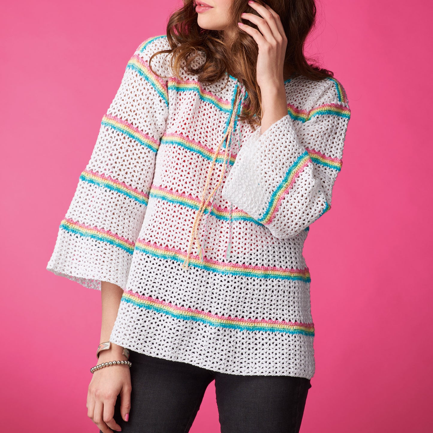 Woman wearing a white crochet top with colorful stripes on a pink background