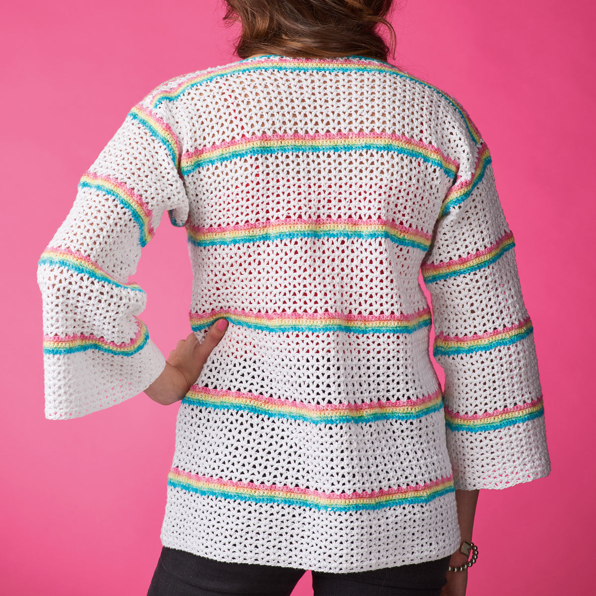White crochet cardigan with colorful stripes on a pink background