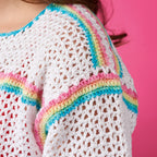 Close-up of a white crochet garment with colorful trim against a pink background