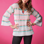 Woman wearing a white crochet top with colorful stripes on a pink background