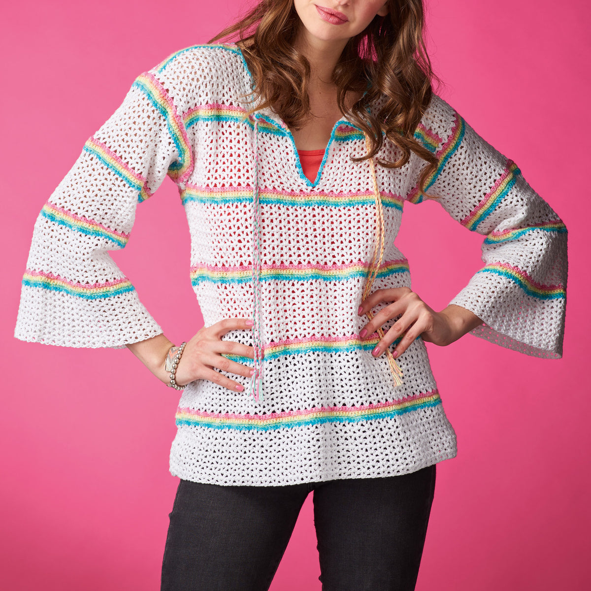 Woman wearing a white crochet top with colorful stripes on a pink background