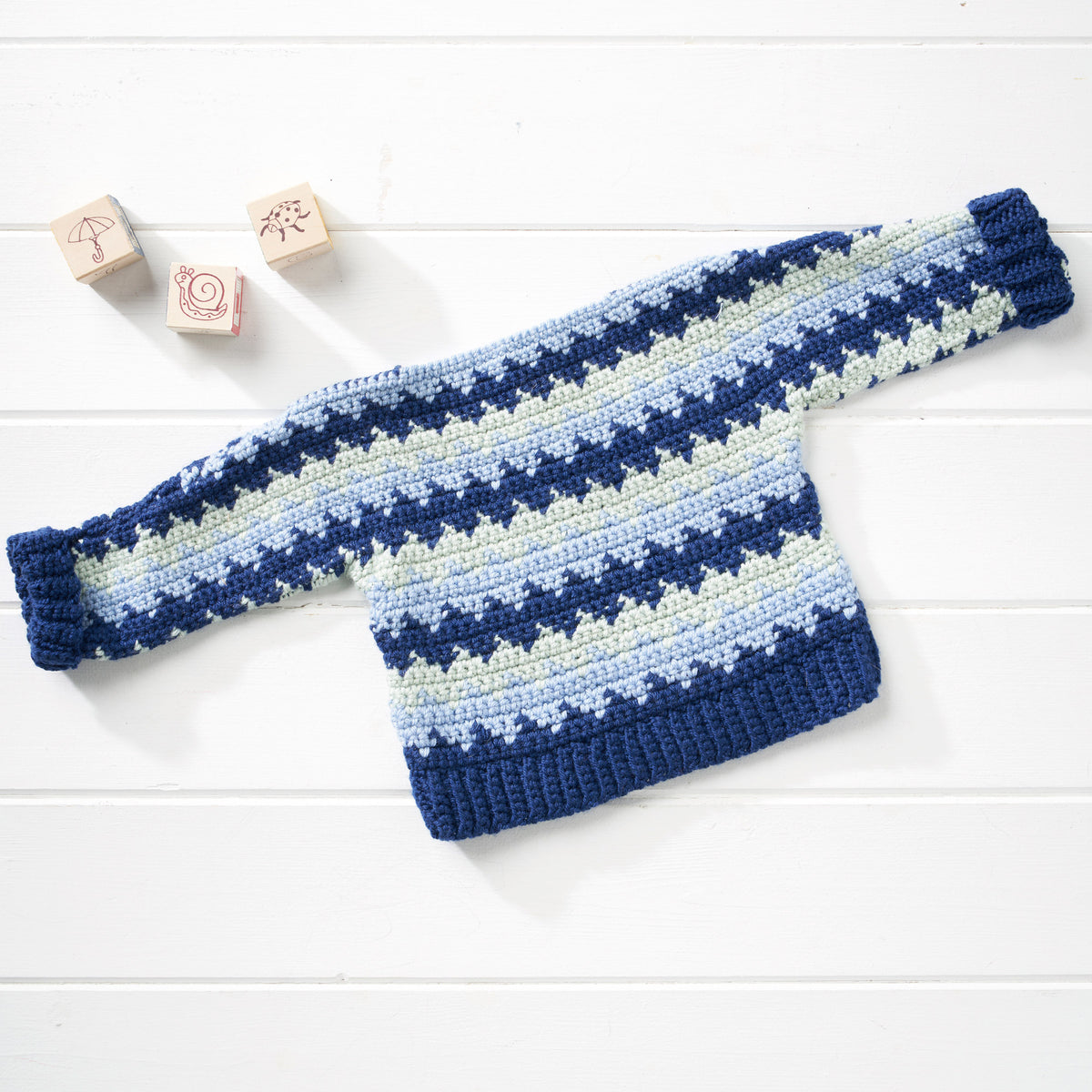 Blue and white striped baby sweater on a light wooden surface with wooden blocks.