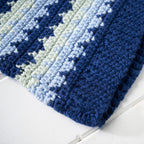 Close-up of a blue and green striped knitted blanket on a white surface
