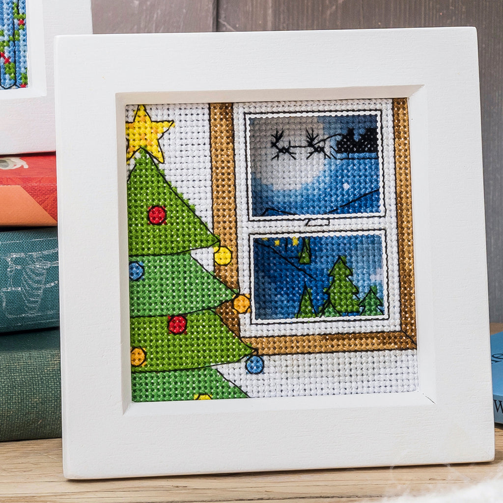 Cross-stitched Christmas scene with a tree and window view on a white background