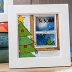 Cross-stitched Christmas scene with a tree and window view on a white background