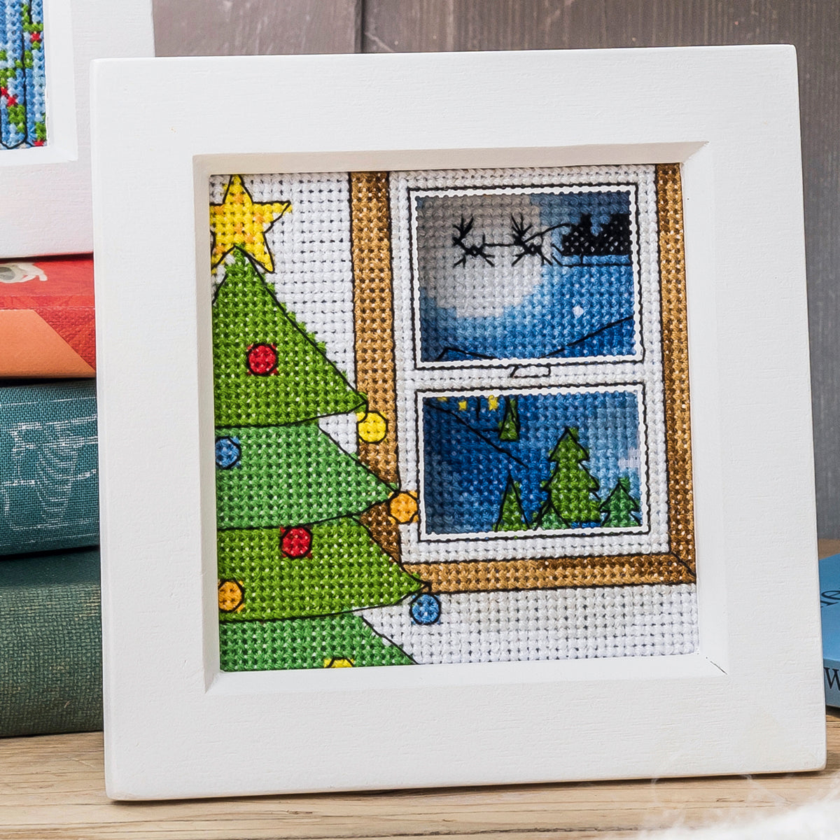 Cross-stitched Christmas scene with a tree and window view on a white background