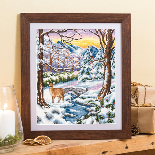 Framed cross-stitch art of a winter scene with a deer and mountains.