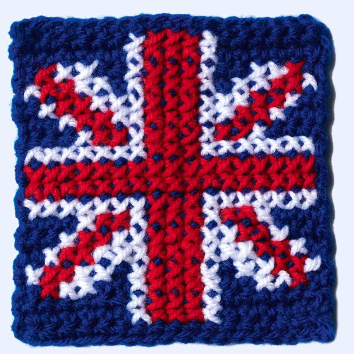 Crocheted patch resembling a Union Jack flag with red, white, and blue yarn. The textured surface gives a cozy and handmade feel.