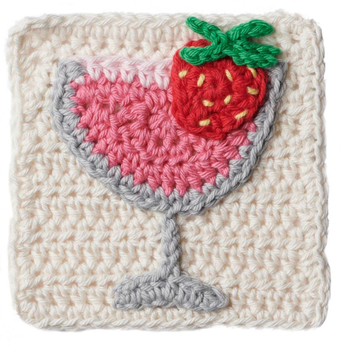 Crocheted square featuring a pink cocktail glass with a gray rim and base, topped with a red strawberry and green leaves. Cream background. Playful vibe.