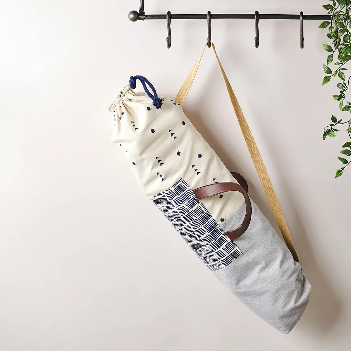 Yoga mat bag with strap hanging on a hook against a white wall.