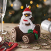 Knitted penguin decoration on a roll of brown paper with a Christmas tree in the background