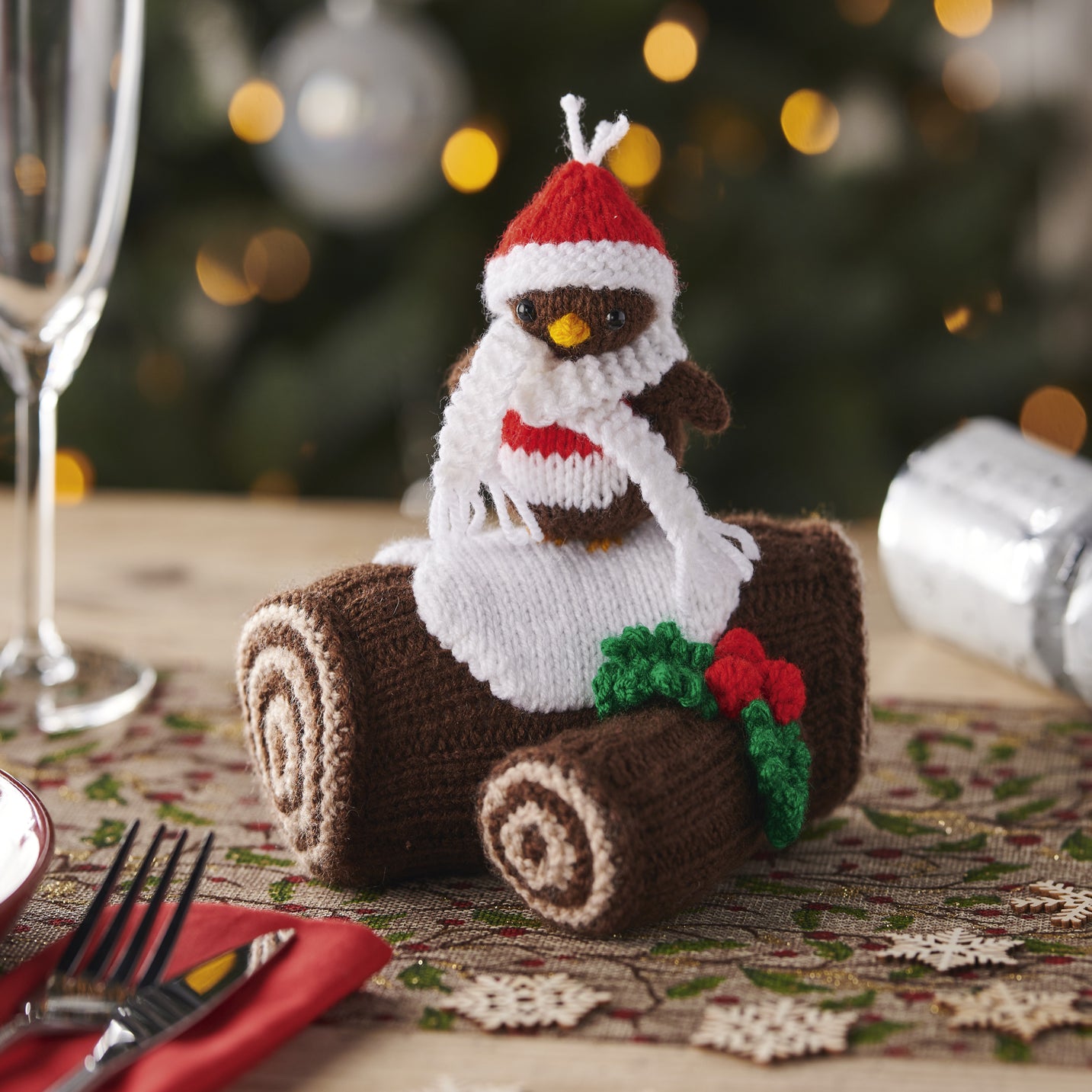 Knitted penguin decoration on a roll of brown paper with a Christmas tree in the background
