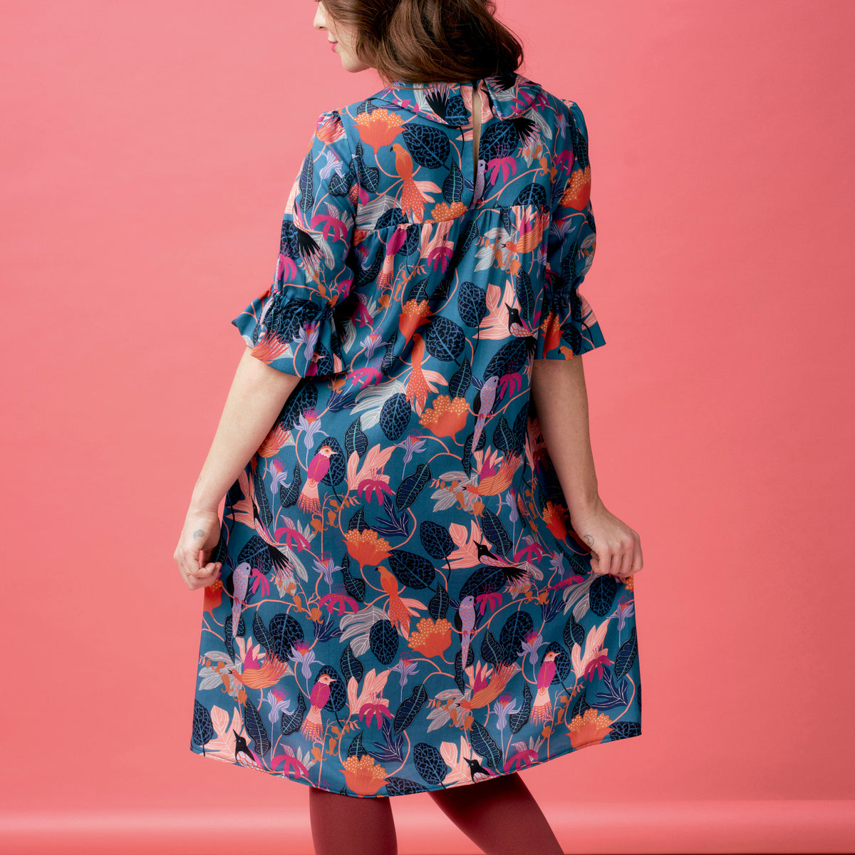 Woman wearing a colorful floral dress against a pink background