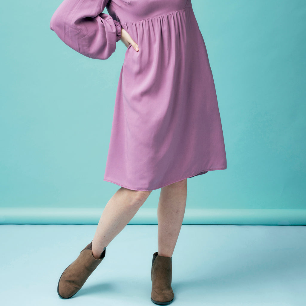 Person wearing a purple dress with brown boots on a light blue background