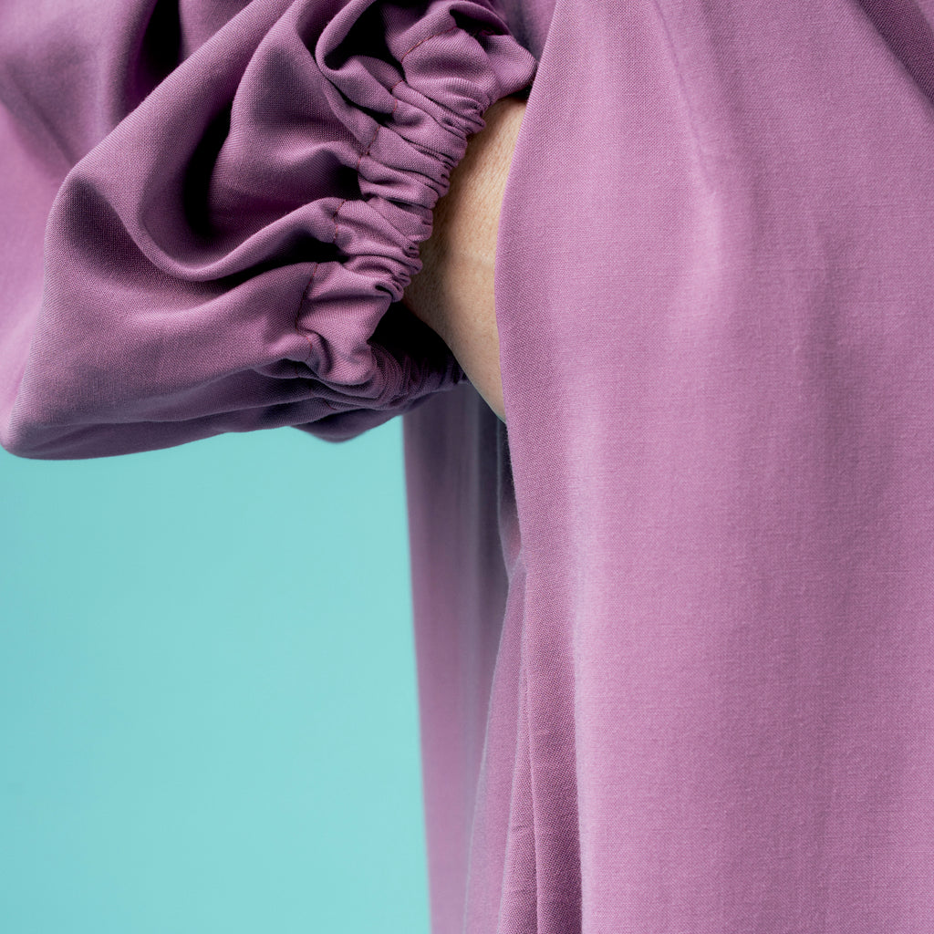 Close-up of a person wearing a light purple dress against a teal background