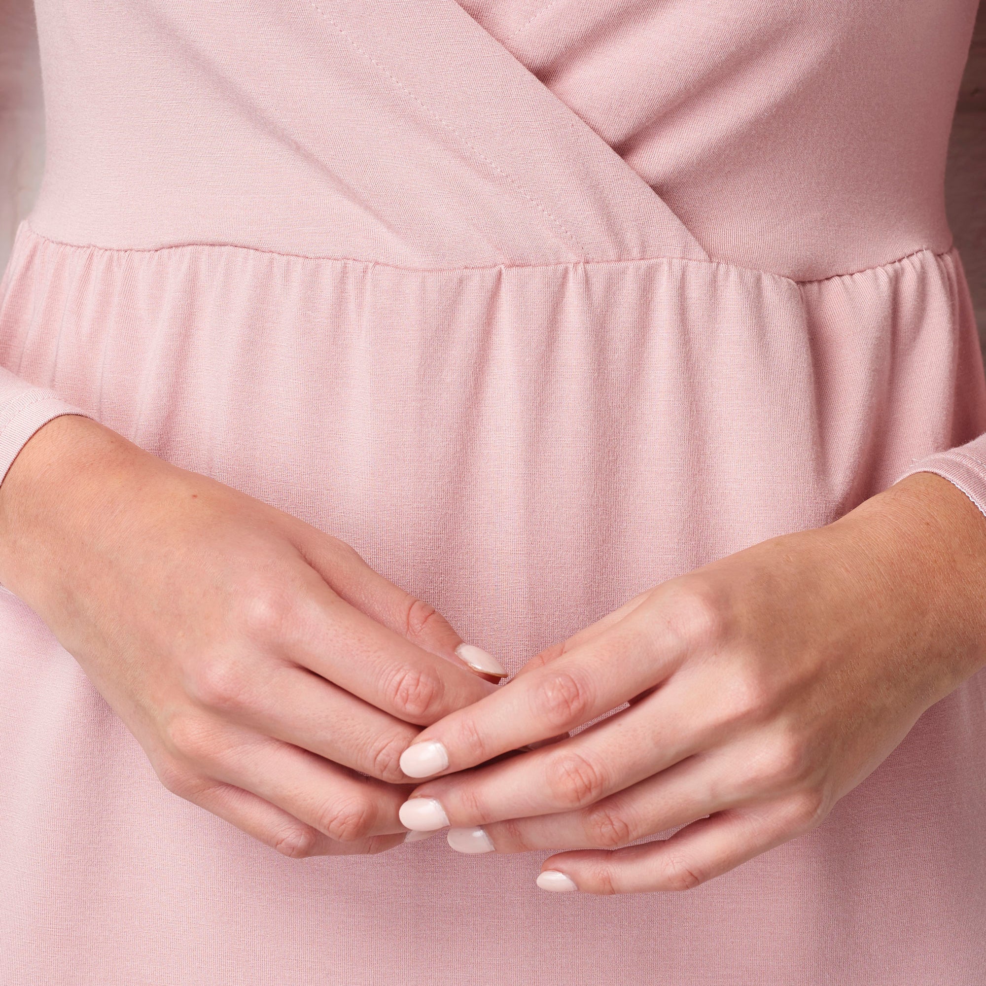 Close-up of hands with light nail polish against a pink fabric background