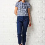 Person wearing a blue and white checkered shirt and navy pants against a white brick wall.