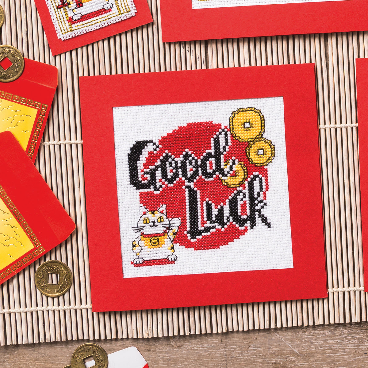 Cross-stitched design with 'Good Luck' text and a cat on a red background, surrounded by decorative items.