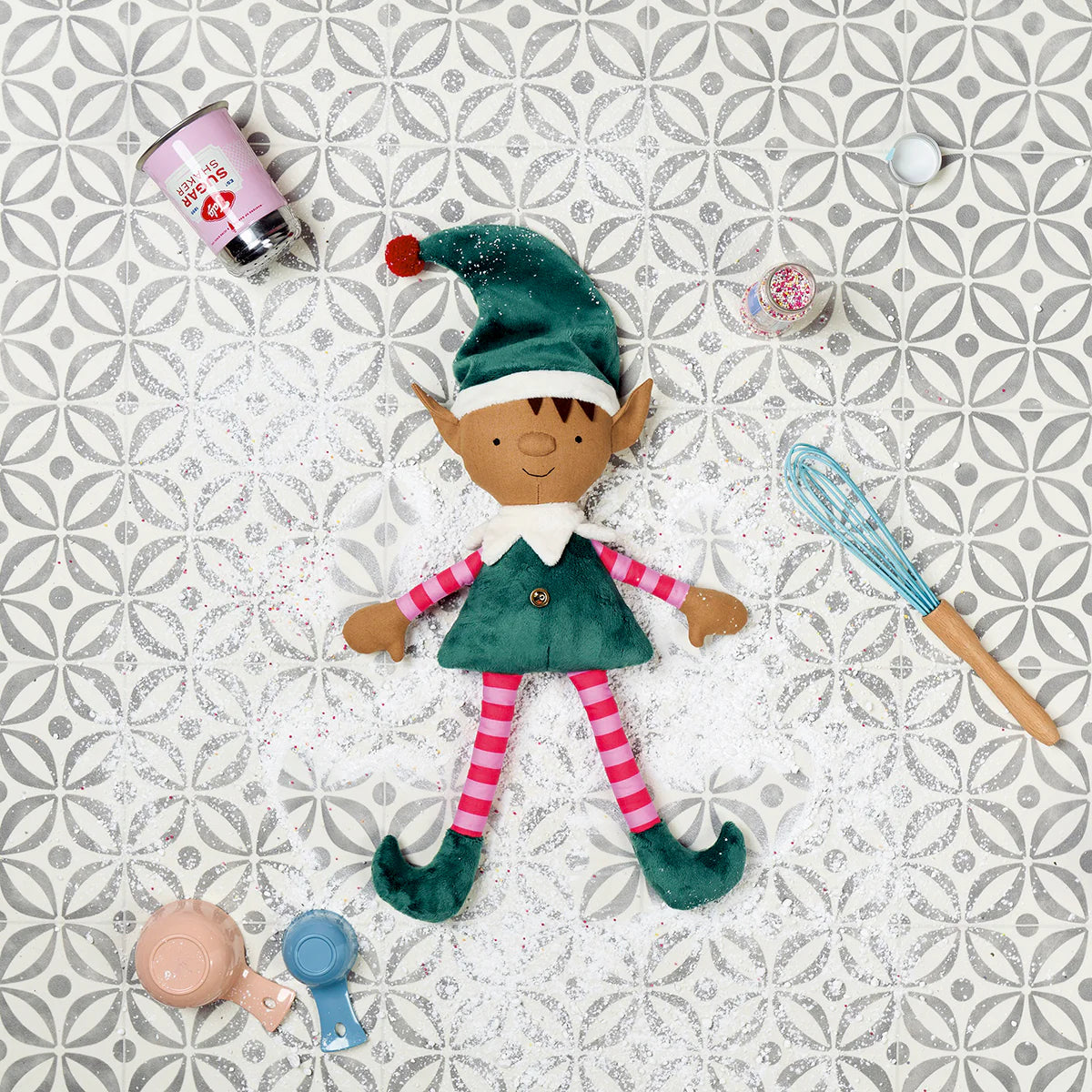 Elf doll with kitchen utensils on a patterned tile background