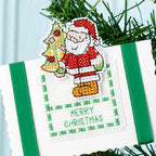 Cross-stitched Christmas ornament with Santa Claus and tree on a white background