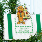 Cross-stitched gingerbread man ornament with a Christmas tree on a white background.
