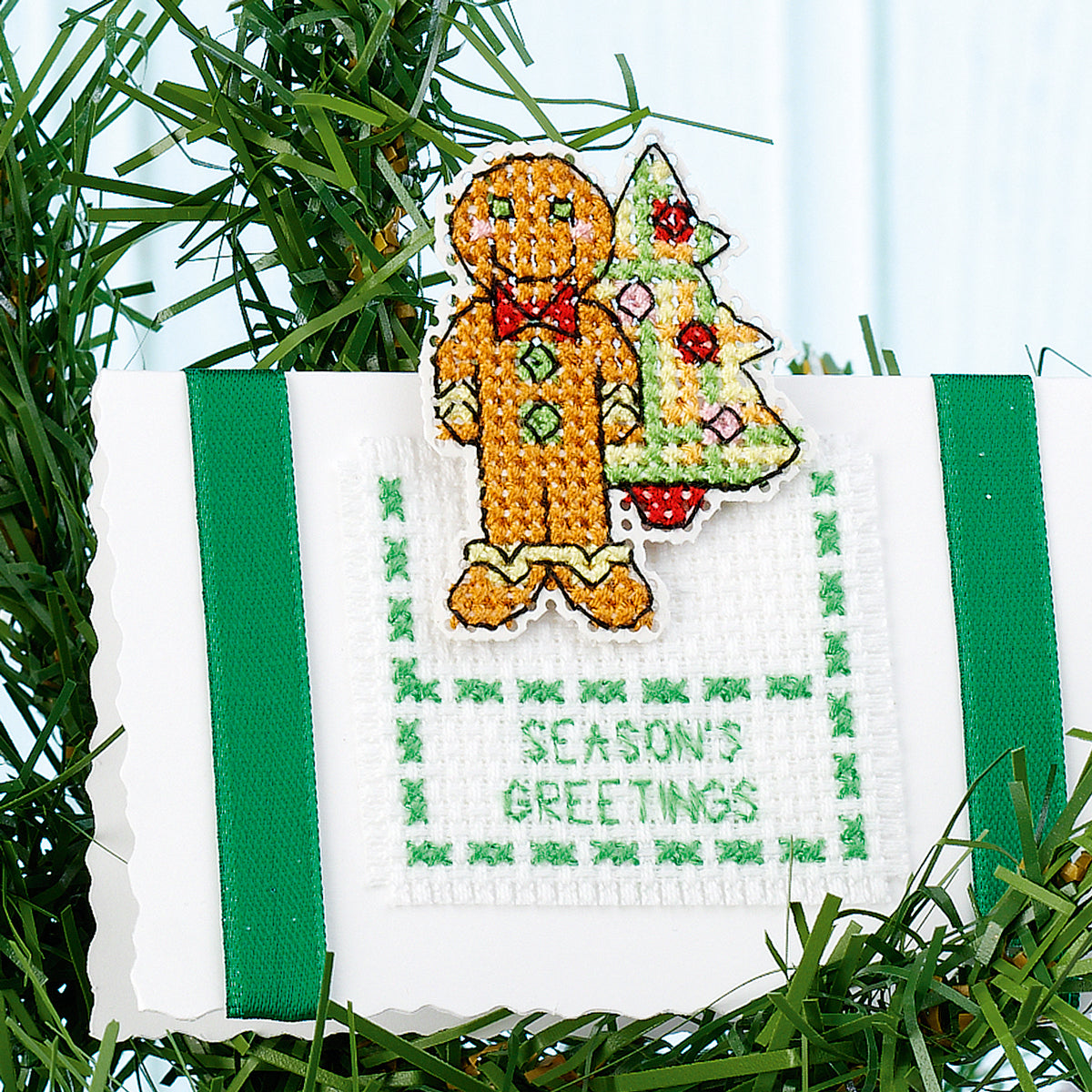 Cross-stitched gingerbread man ornament with a Christmas tree on a white background.